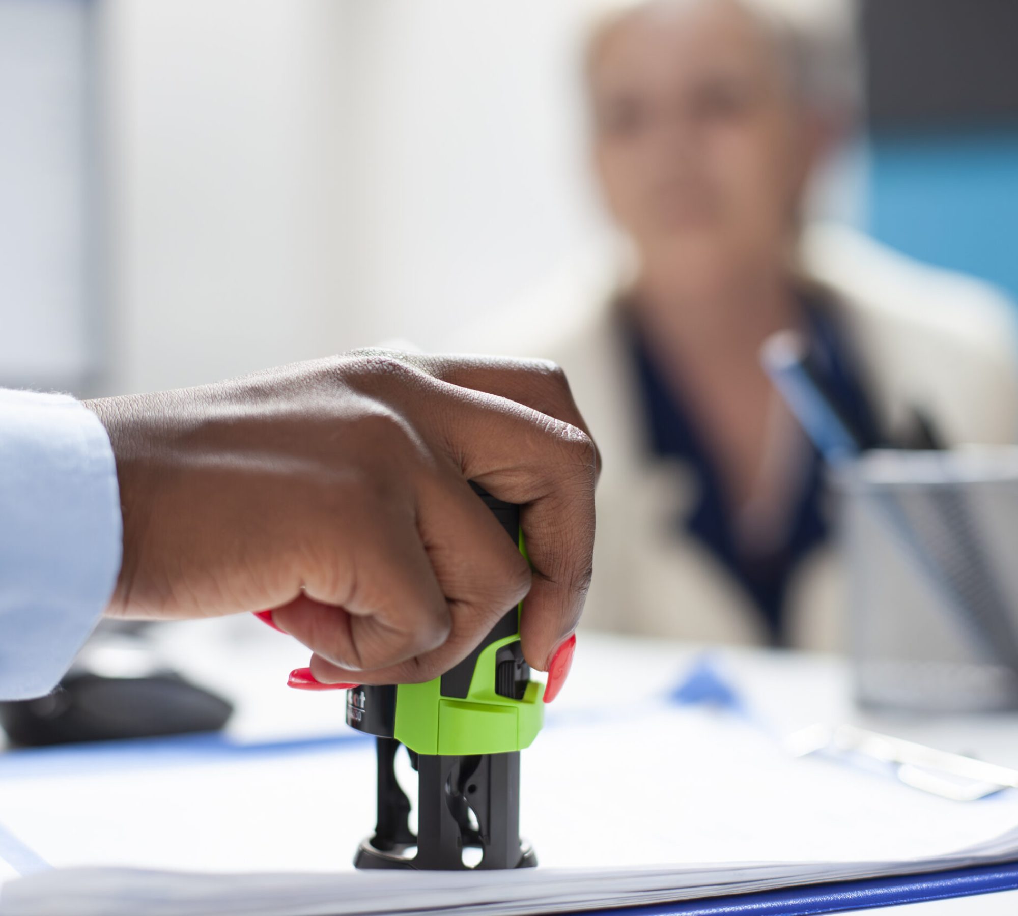 Selective focus on hand of black healthcare specialist applying stamp on document as senior woman watches attentively. Elderly patient waits as african american doctor completes her medical documents.